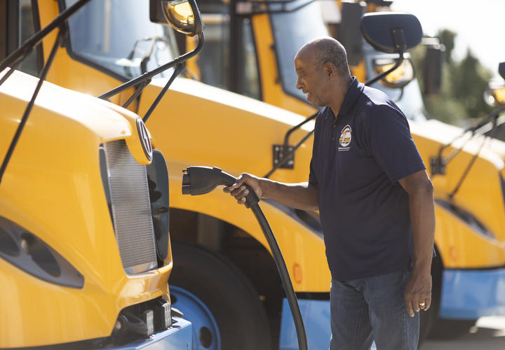 Conductor de autobús escolar enchufando un autobús escolar amarillo eléctrico para cargarlo