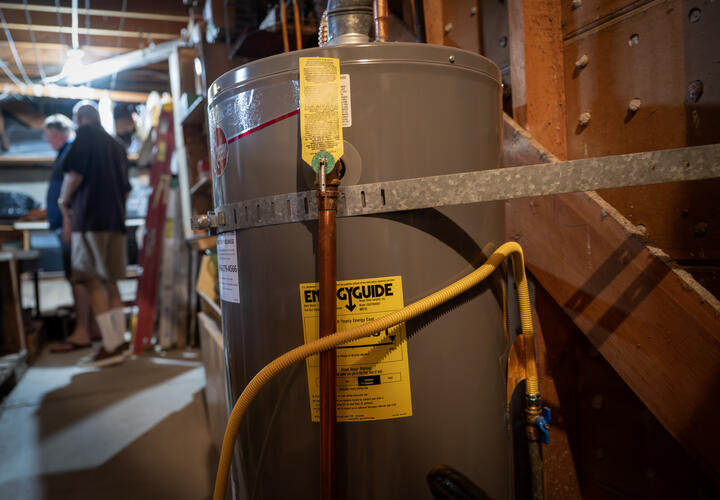 An image of a hot water heater, with two people talking in the background.