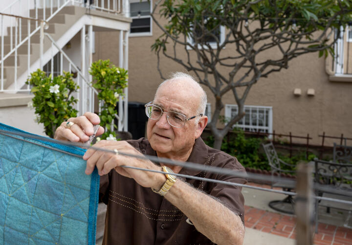 A man pins a bright blue piece of cloth to a clothesline in his backyard.
