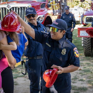 Image of female firefighter placing a toy hat onto a young child