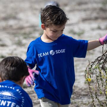 Un niño pequeño sostiene desechos vegetales durante un evento voluntario en Mission Bay, San Diego.