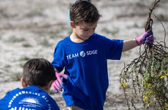 Un niño pequeño sostiene desechos vegetales durante un evento voluntario en Mission Bay, San Diego.