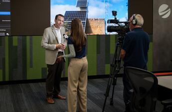 A media interview takes place at SDG&E's WCRC with illuminated screens in the background.