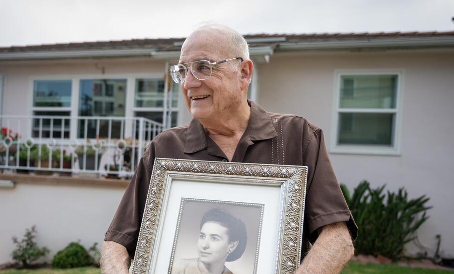An elderly man, holding a black-and-white photo of his mother, stands in front of his Little Italy home. 