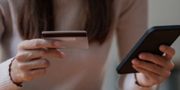A photo of a woman holding her mobile phone in one hand, and a credit card in the other. 
