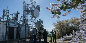 People stand in a gathering around weather-monitoring technology infrastructure.