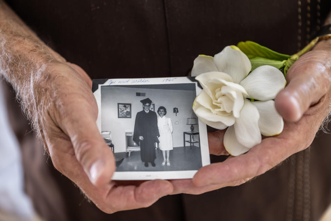 Hands holding a black-and-white photo, alongside a white gardenia. 