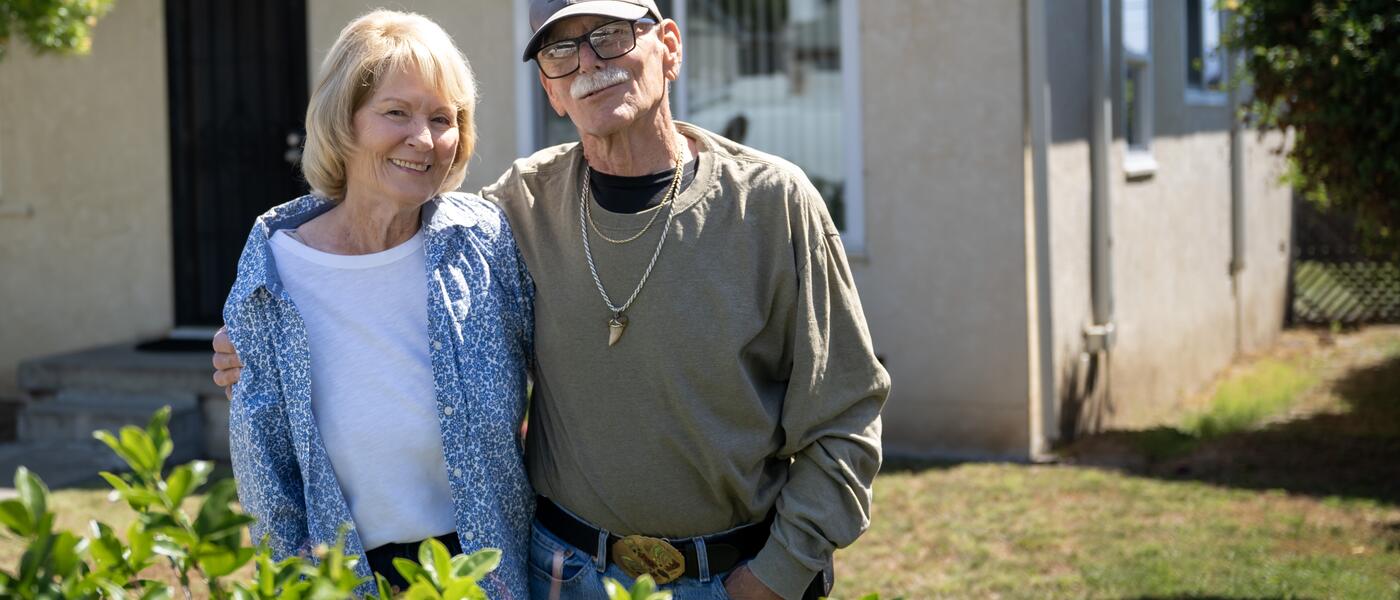 A man and women pose for a photo outside their home.