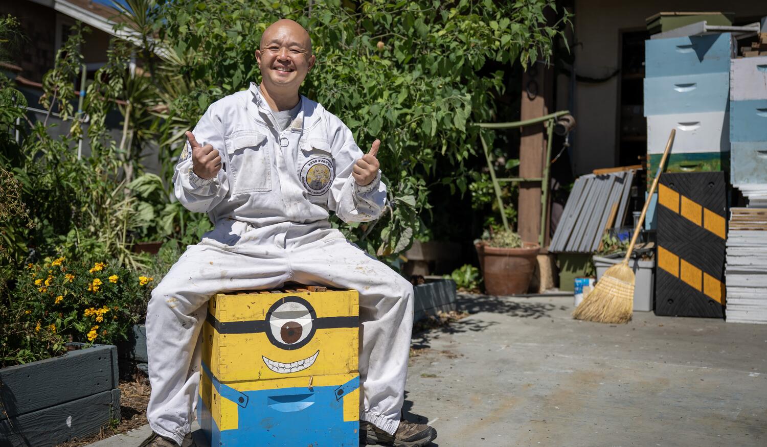 Dan the Bee Man poses for a photo, sitting on a colorful wood box and giving a thumbs up sign.