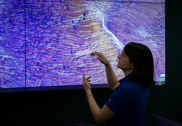 Image of female employee presenting weather data in front of a large display screen.