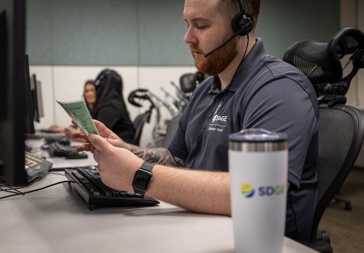 Male SDG&E employee reviews a fact sheet whole answering a customer call. 