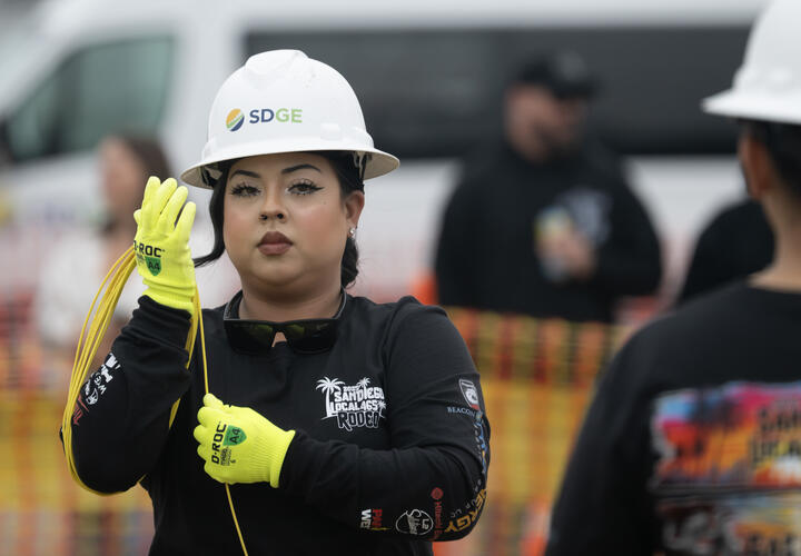 A female member of the gas crew wearing an SDG&E hard hat rounds up rope around her arm.