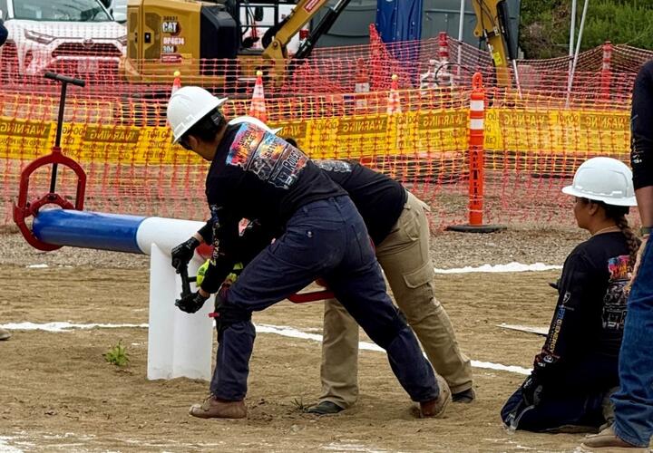 Tres mujeres que visten cascos de SDG&E participan en el rodeo de trabajadores de línea.