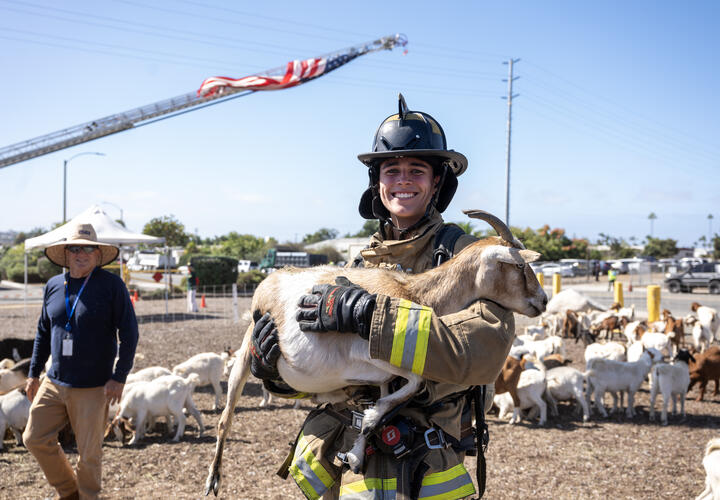A firefighter, smiling, holds a goat.