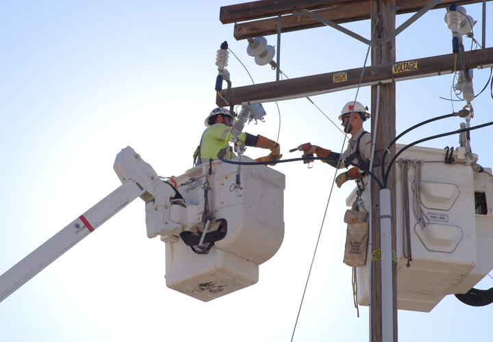 two line workers conduct electrical operations while elevated in a white bucket truck