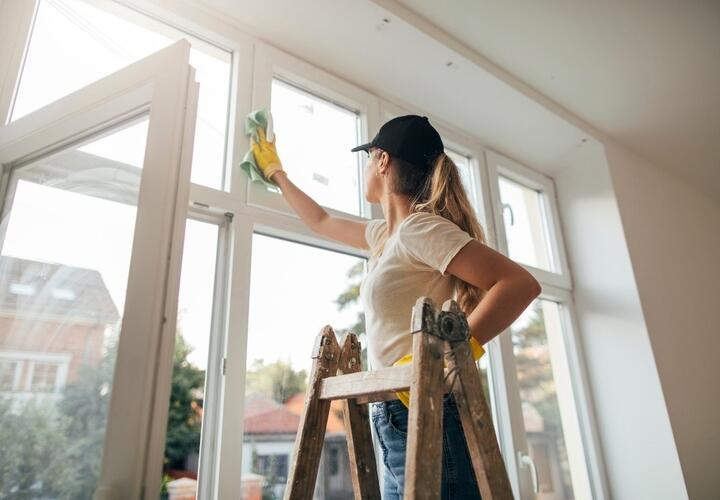 A woman with a ponytail stands on a ladder, cleaning the windows.
