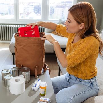 Woman packing an emergency kit that includes medicine, first aid, canned food and toilet paper