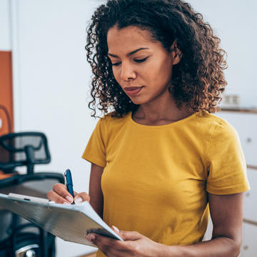 Woman in a yellow shirt with a checking a list on a clipboard