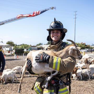 A firefighter, smiling, holds a goat