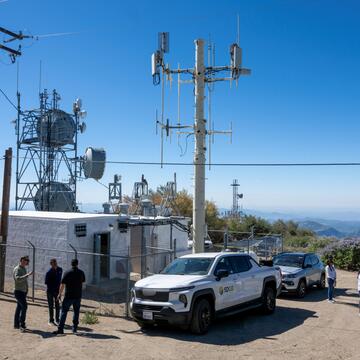 Communications and weather monitoring equipment installed on a mountain site, with utility vehicles and staff nearby.