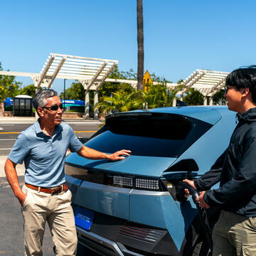 Two men talk as the younger of the two charges his electric vehicle.