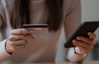 Una fotografía de una mujer sosteniendo su teléfono móvil en una mano y una tarjeta de crédito en la otra.