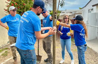 A group of employees wearing blue shirts plants a tree.