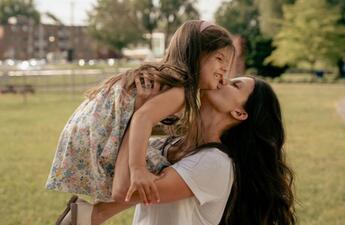 A woman holding her small child in a scenic, park-like setting. 