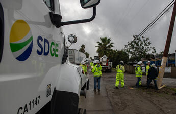 An SDG&E vehicle with field workers wearing bright yellow vests in the background.