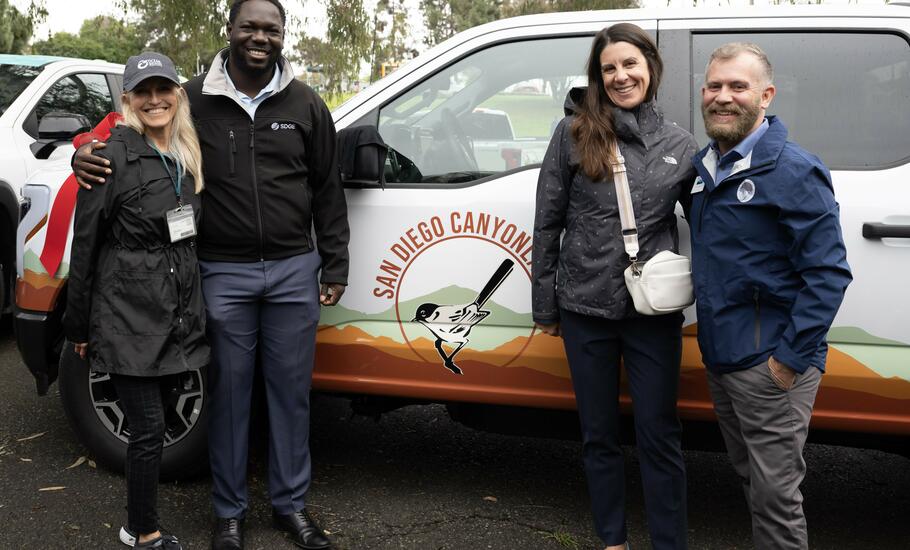 Event attendees pose for a photo with two donated electric vehicles in the background