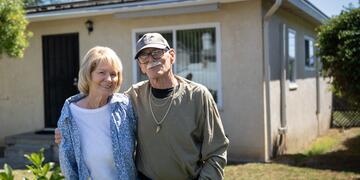 A man and women pose for a photo outside their home.