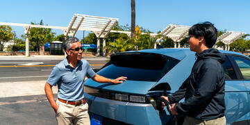 Two men talk as the younger of the two charges his electric vehicle.