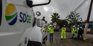 An SDG&E vehicle with field workers wearing bright yellow vests in the background.